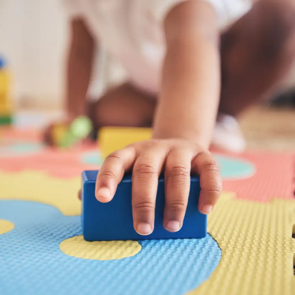 Nahaufnahme einer Kinderhand die gerade mit einem Baustein spielt